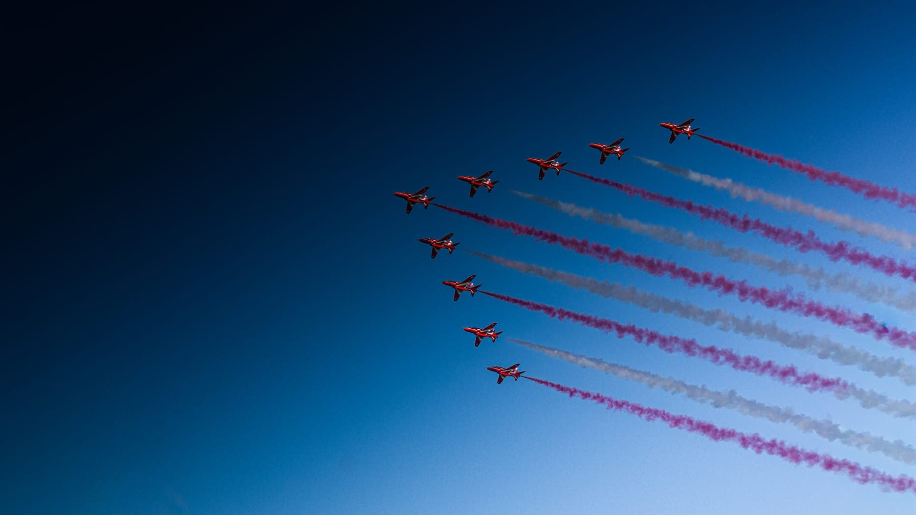 RAF Red Arrows in nine-ship formation trailing red and white smoke over Boston